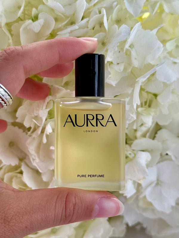 AURRA pure perfume bottle held in front of white flowers