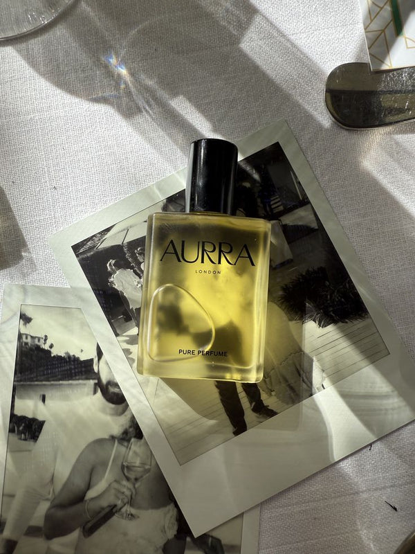 Aurra perfume bottle on a textured surface with black and white photos underneath