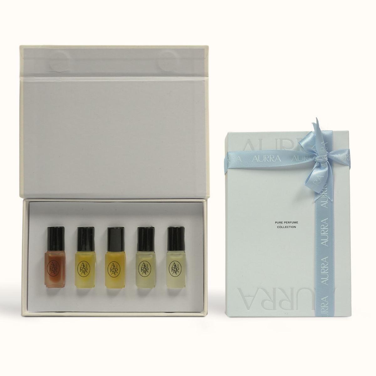 A boxed fragrance gift set on a clean white background, showing an open white box with five perfume sample vials and a matching closed box with a pale blue ribbon and bow. The visible text includes AURRA.